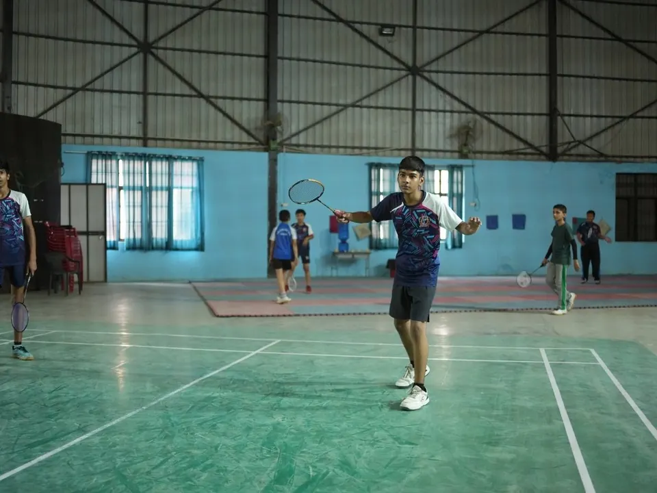 A student plays a shot in an indoor badminton hall