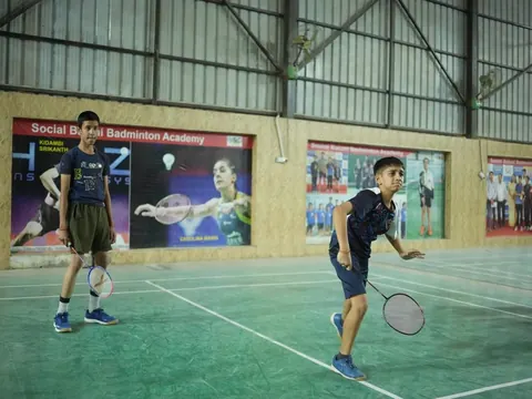 Two students play badminton in an indoor hall