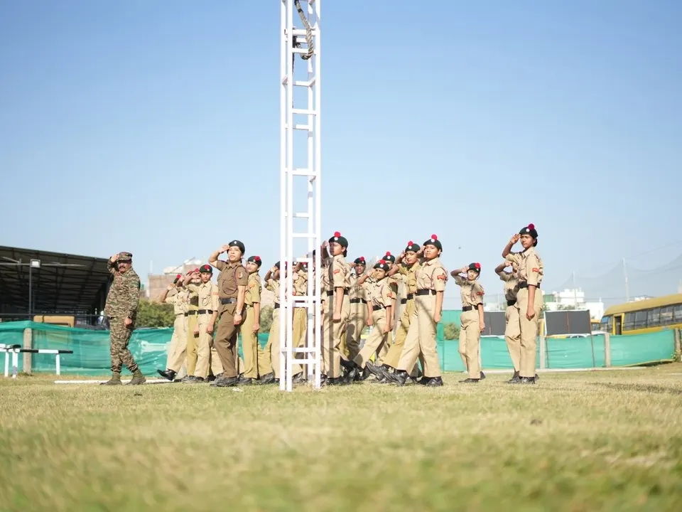 Students in uniform salute during a drill session on the ground