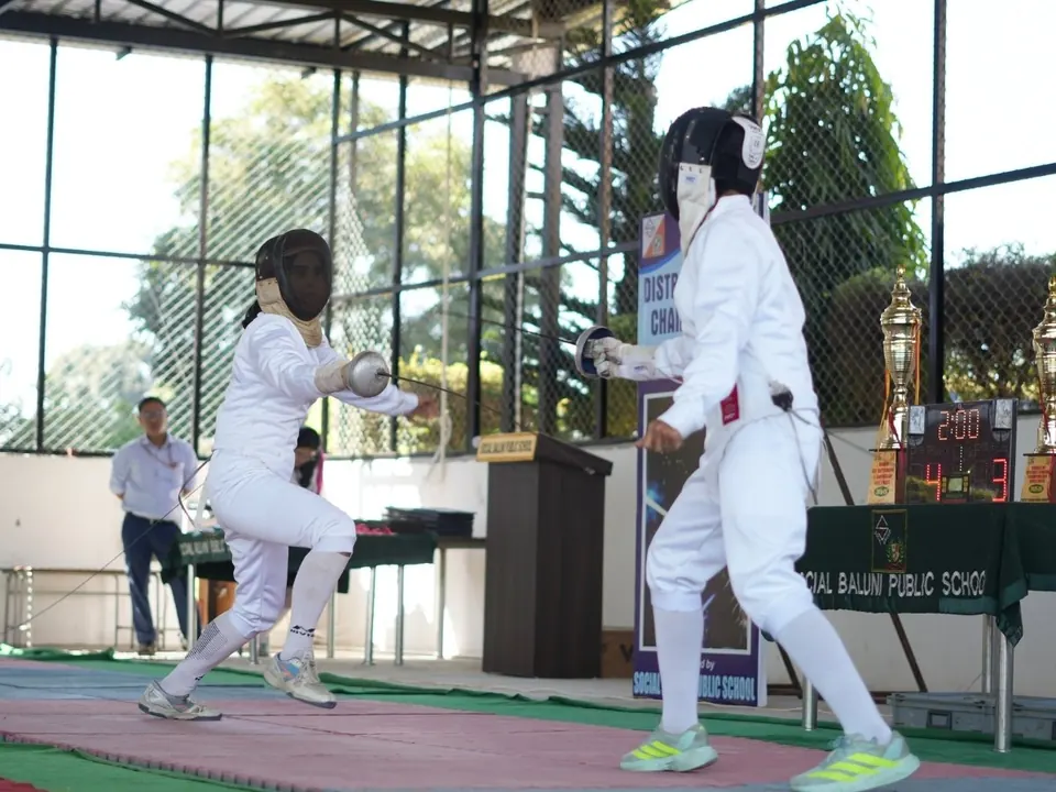 Two fencers in white kit compete on a fencing piste