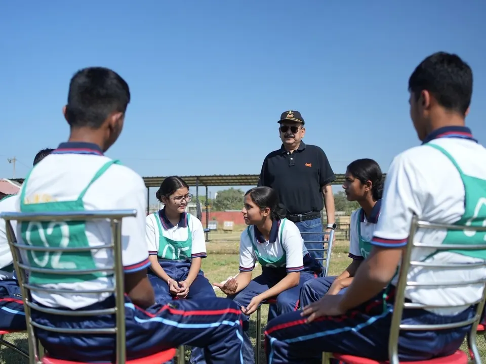 Students sit in a circle on the ground for a group discussion while an instructor watches