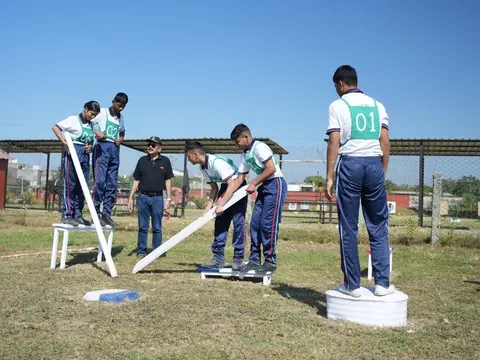 Students wearing numbered bibs use a plank to cross an outdoor obstacle as a team